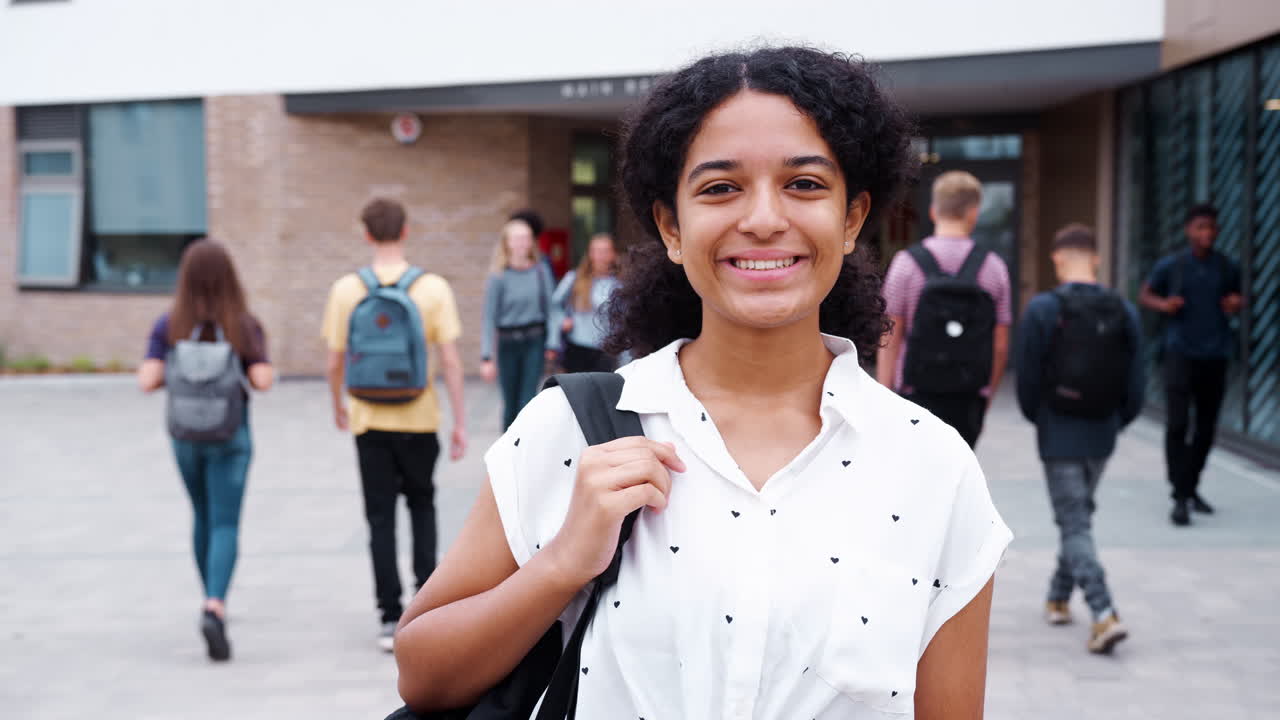 retrato de una estudiante de secundaria sonriente fuera del edificio de la universidad con otros estudiantes adolescentes en el fondo
