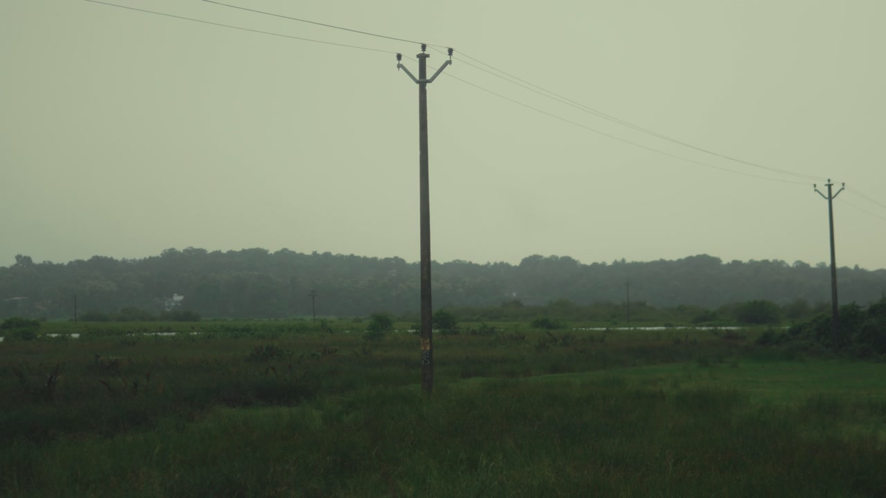 Electric poles and power lines crossing a green rural field under cloudy sky calm countryside atmosphere