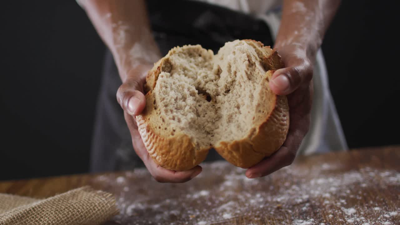 Video of cook holding loaf of bread on black background