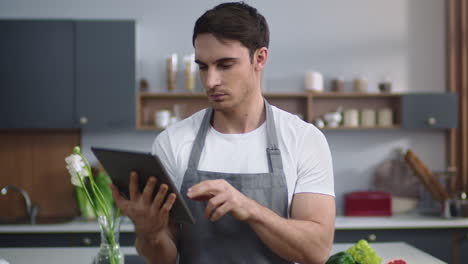 man chef reading recipe on tablet at home kitchen. man chef browsing internet.