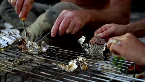 cooking burgers wrapped in aluminum foil in a fireplace