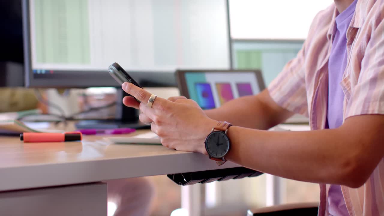 sección media de masculino asiático creativo usando teléfono inteligente en el escritorio en una oficina casual, cámara lenta.
