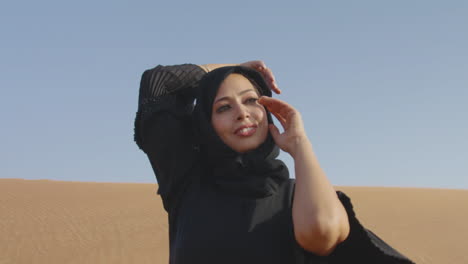 muslim woman wearing traditional black dress and hijab posing in a windy desert 1