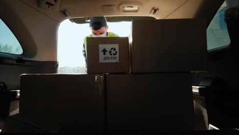 Person-in-a-mask-loads-boxes-of-medicines-in-the-trunk-of-the-car