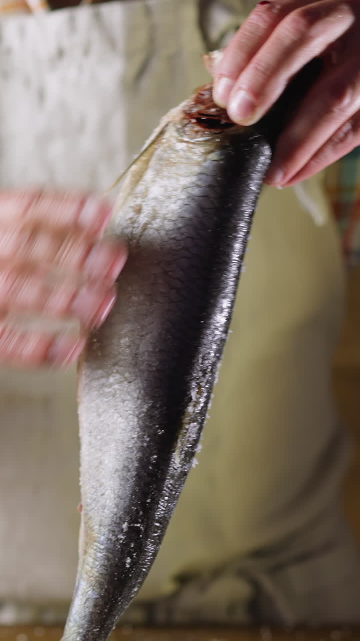 Man in apron removes salt from tasty fat marinated herring on wooden background in kitchen close view. Healthy nutrition of seafood products