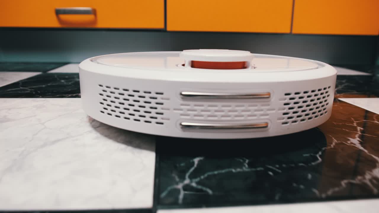 el aspirador robot limpia en la casa moderna en el piso de azulejos en la cocina