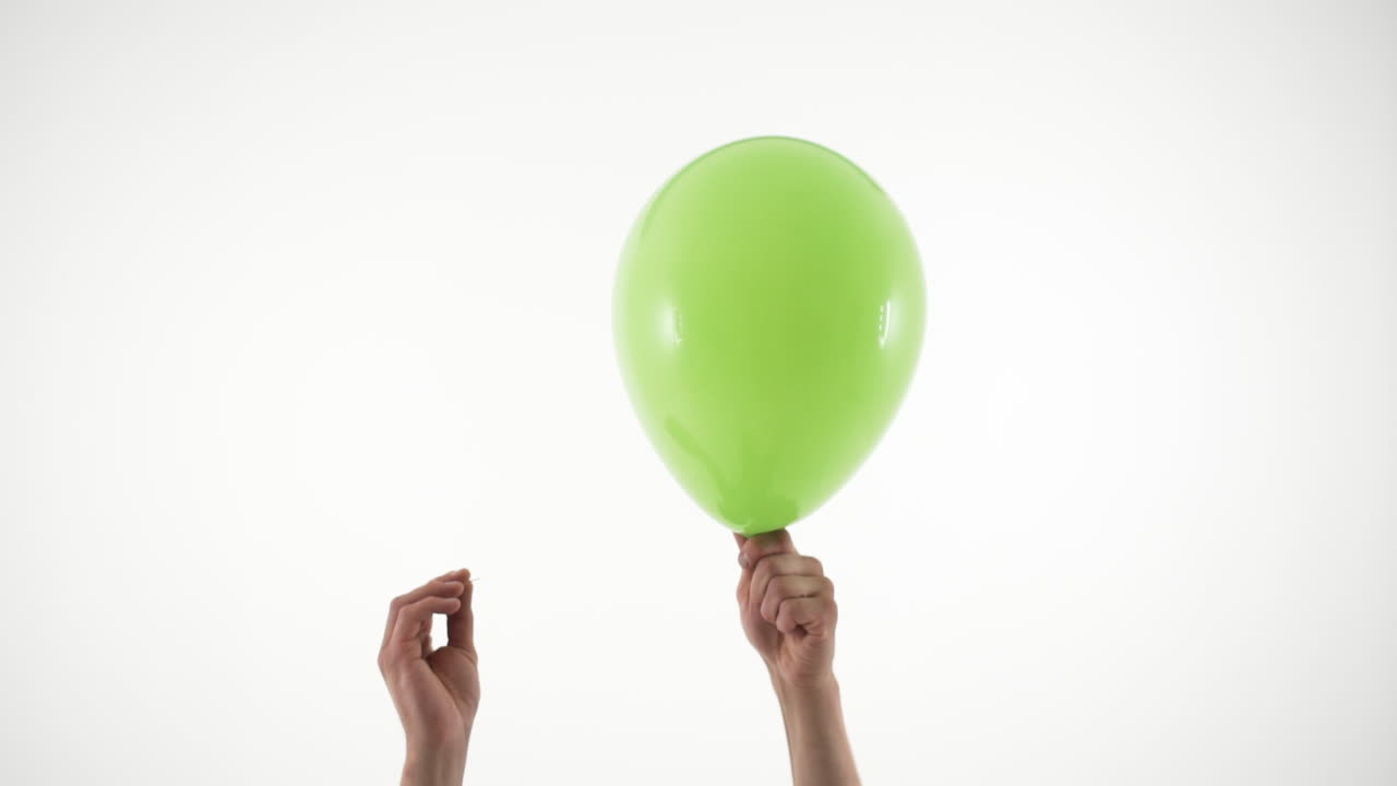 Due mani fanno scoppiare un palloncino verde con un ago
