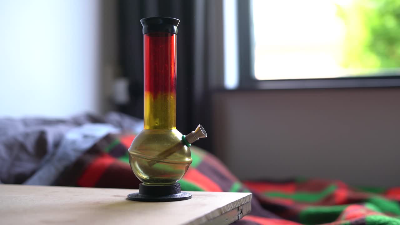 bong rojo y amarillo parado al lado de la cama, adicción a las drogas, rutina de hábitos recreativos, primer plano