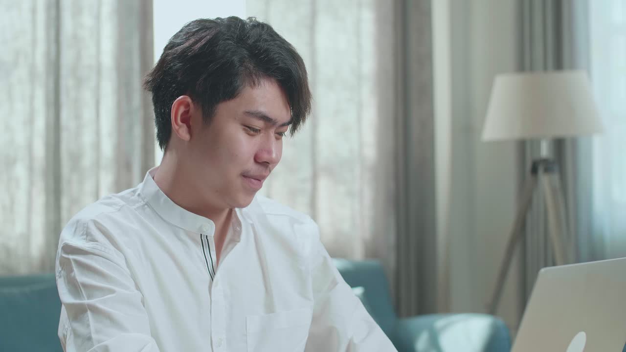 Close Up Of Asian Man Student Look At Camera And Smile While Typing On Computer At Home