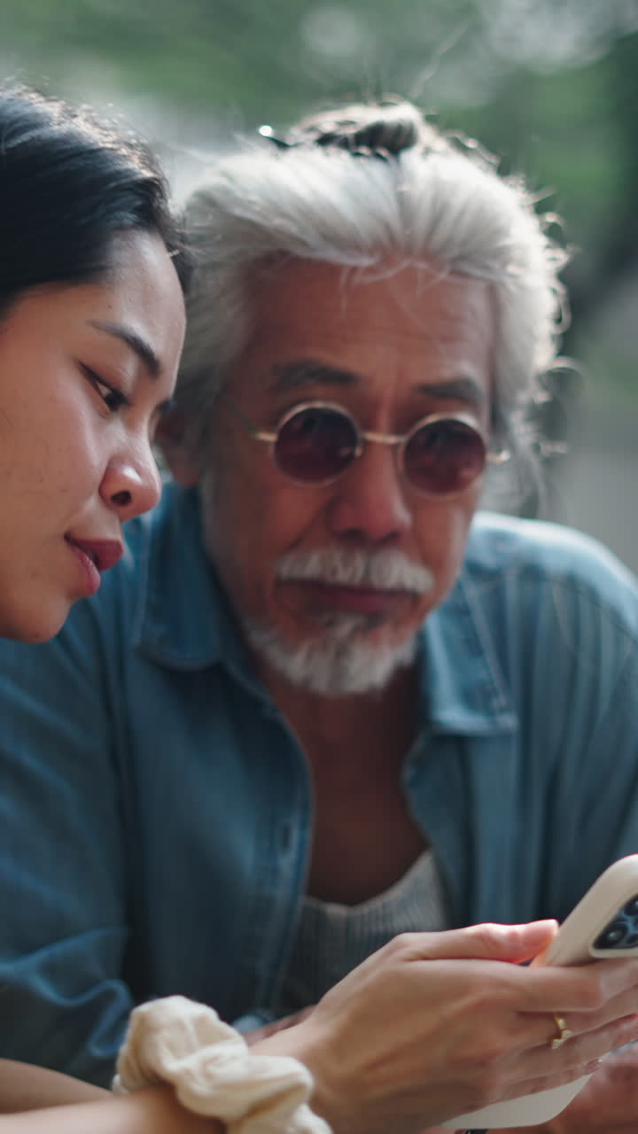 Young Woman and Senior Man Looking at Smartphone Together