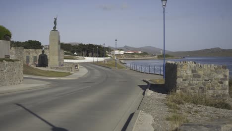 camera pans right, revealing an empty road leading to stanley harbor in the falkland islands under a sunny blue sky