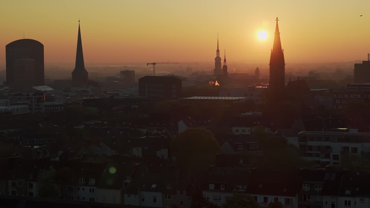 Dortmund City skyline silhouette with orange sunrise, bird flys across static telephoto drone shot