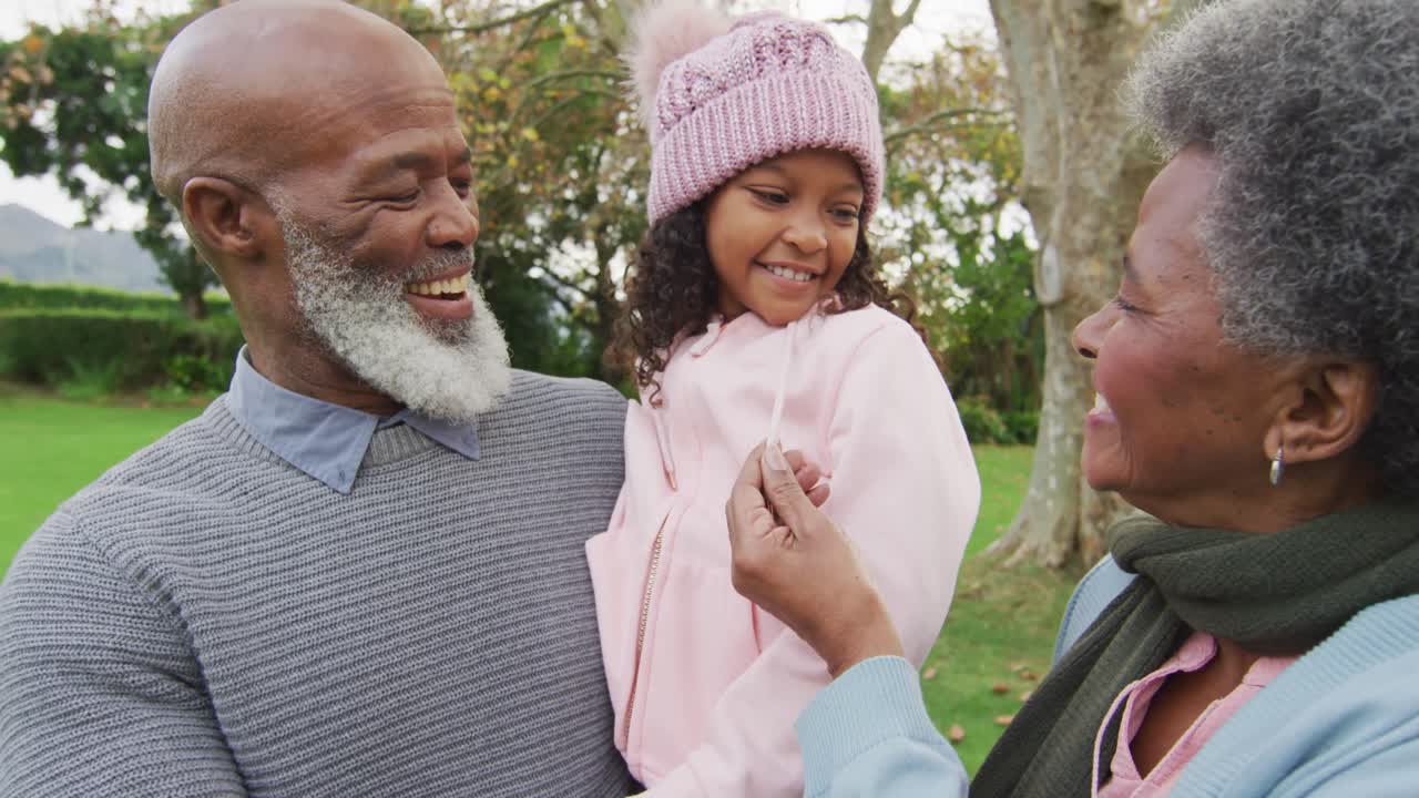 Video of happy african american grandparents, grandfather holding granddaughter in garden