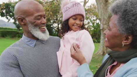 video of happy african american grandparents, grandfather holding granddaughter in garden