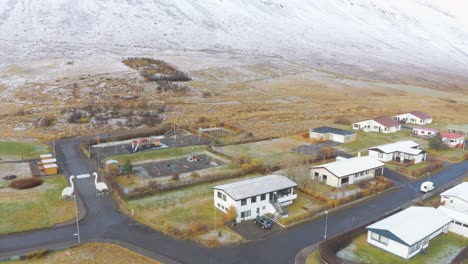 a stunning view of a small town at the foothill of snow-covered mountains surrounded by blue sea - aerial shot