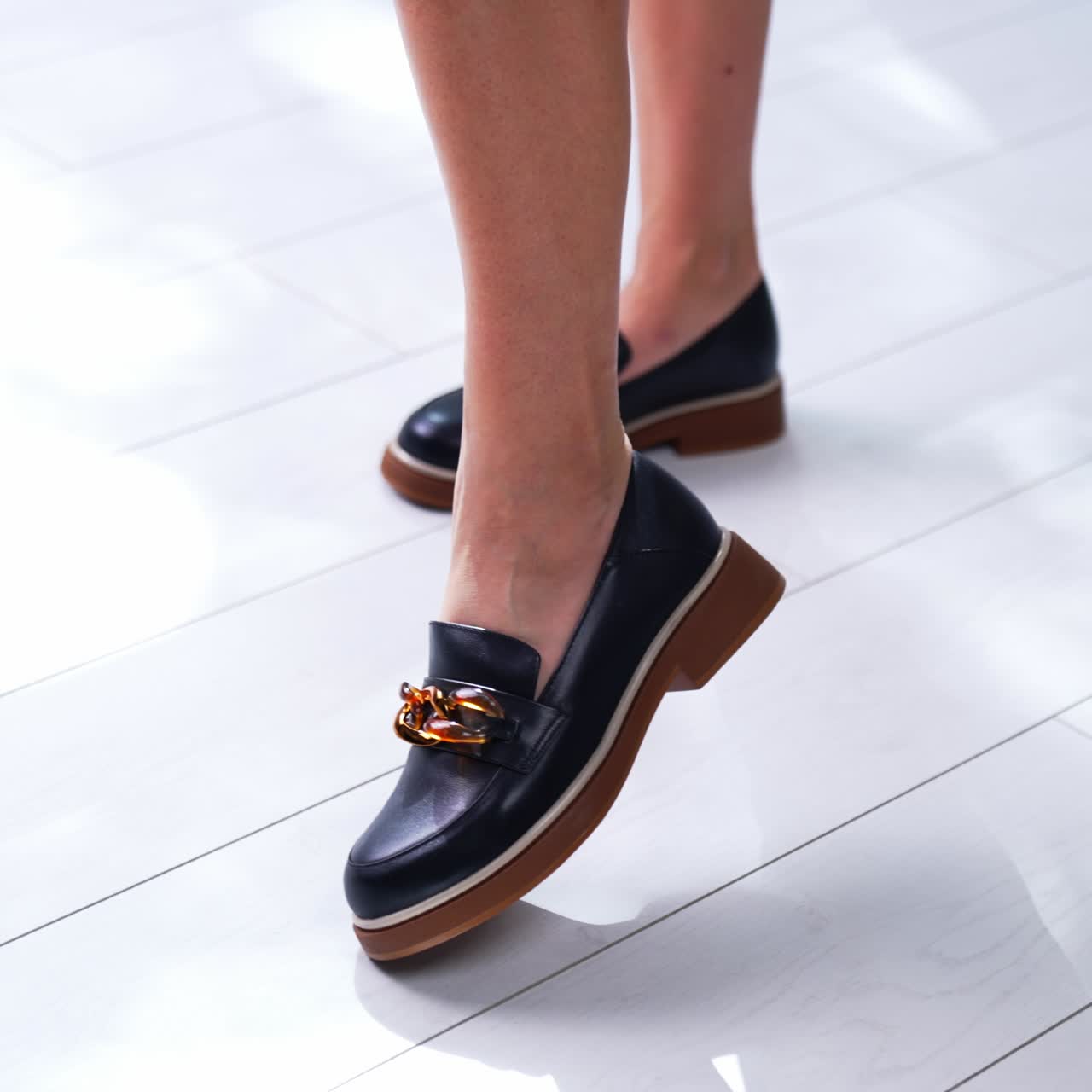 Beautiful black shoes on brown soles with chain decoration. Fashionable loafers on model's feet. Close up. White backdrop