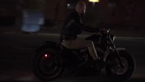 side view of a biker in leather jacket riding motobike by night city street