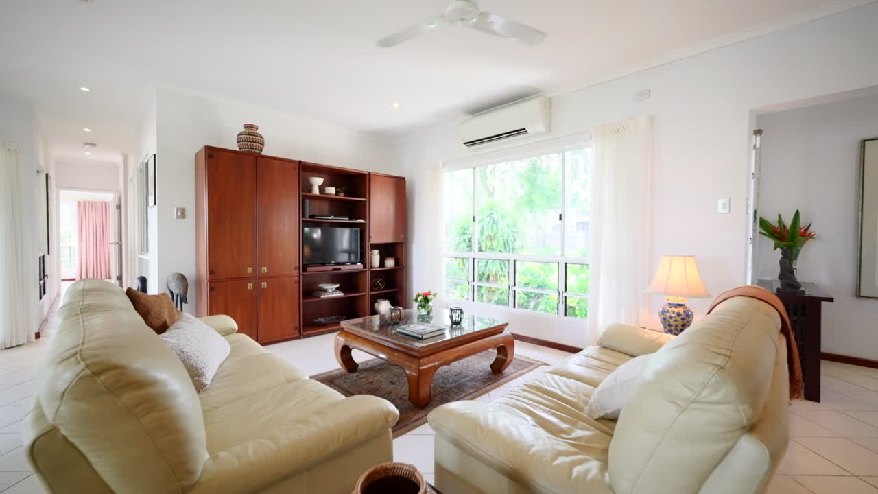 고전적 인 가죽 소파 는 열대 집 의 나무 엔터테인먼트 센터 와 큰 창문 을 둘러싸고 있다