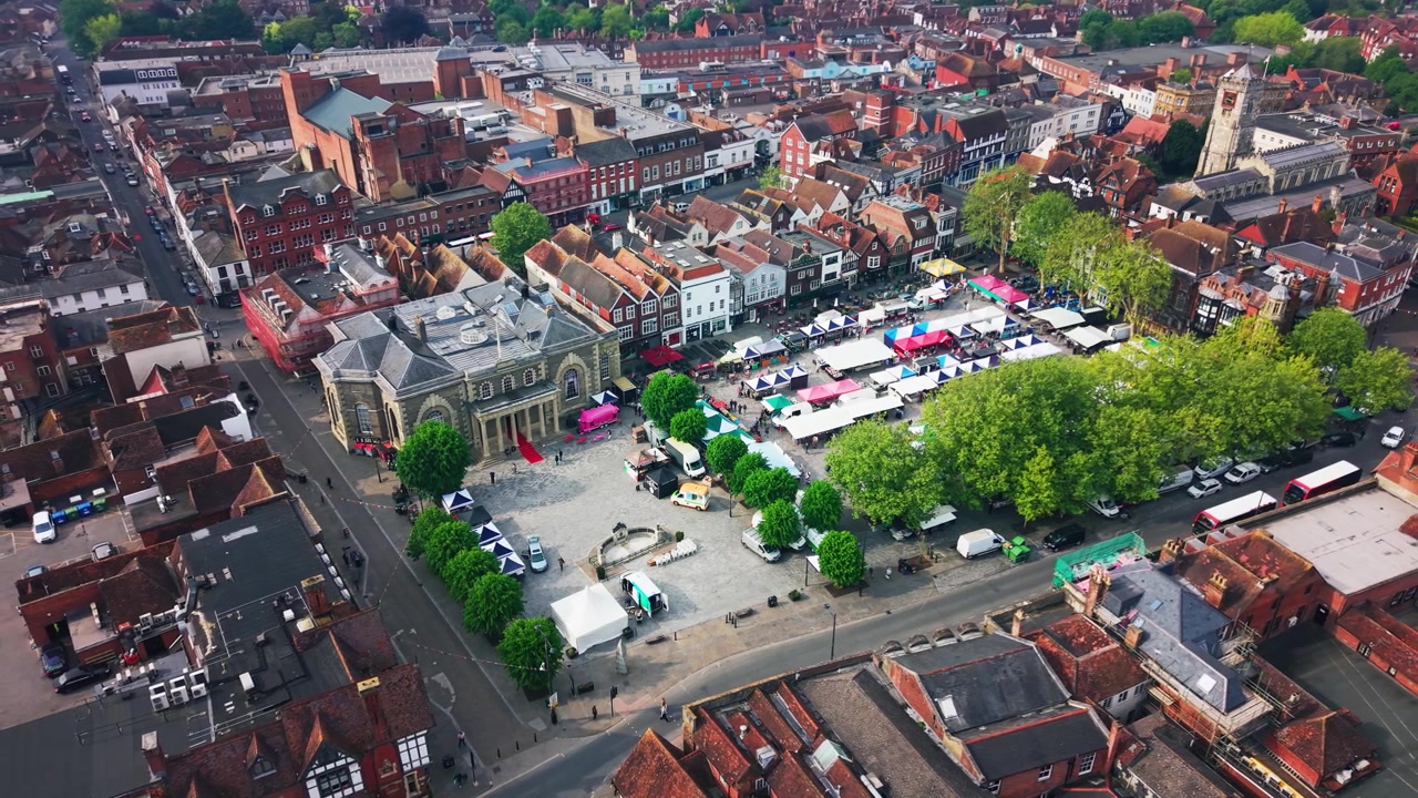 Droneopptak som viser Salisbury Market Square med Guildhall, markedsboder, trær, historiske tak, gater og St Thomas Church i sentrum