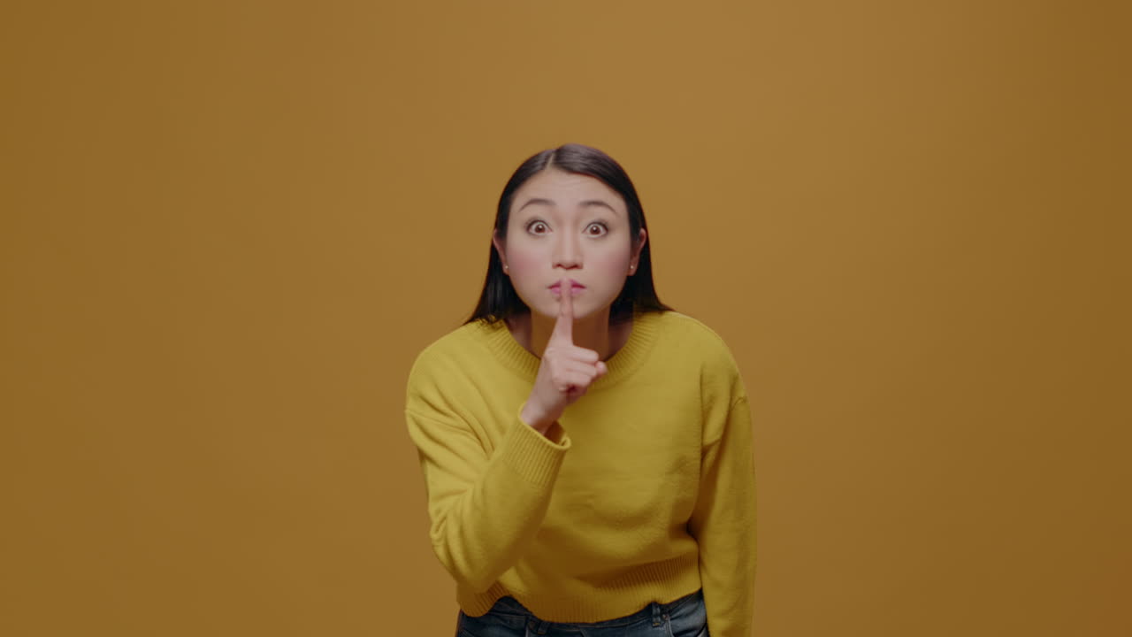 Asian woman doing silent gesture with index finger over lips