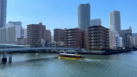 yellow boat cruising on river in urban setting, city buildings in background, clear sky