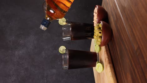 Chilean-Piscola-drink-typical-summer-cocktail-of-Chile-glass-with-ice-wooden-board-lemons-with-selective-focus,-dark-background-vertical-video