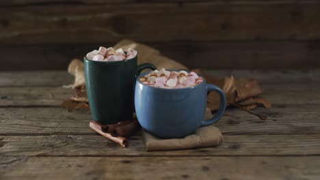 two cups of hot chocolate with marshmallows, autumn leaves and cinnamon sticks on wooden surface