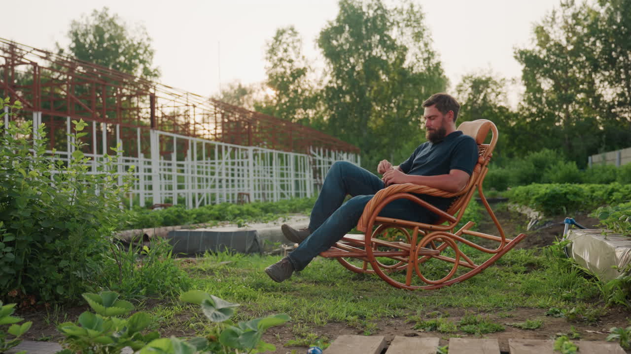 man seated in wooden rocking chair amid greenhouse garden holds steaming cup of herb tea and sips slowly under golden sunset light surrounded by lush greenery rustic atmosphere