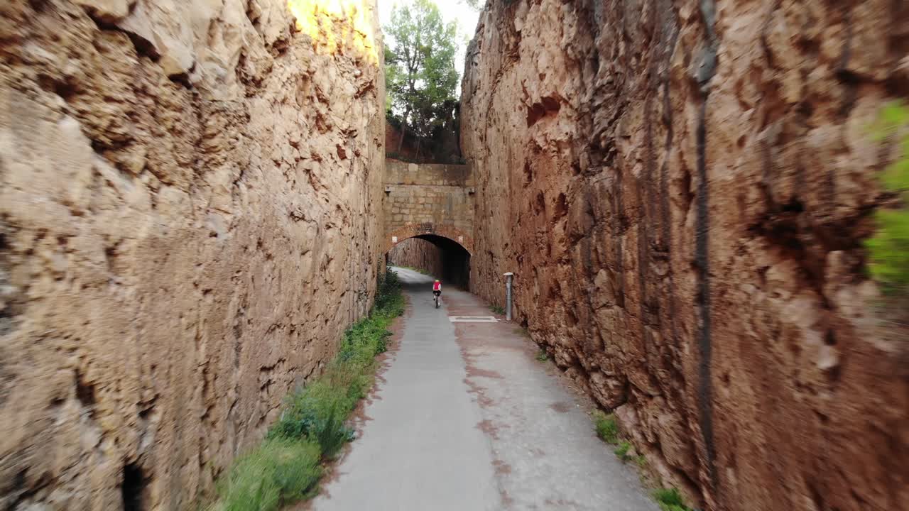 el ciclista se acerca a un túnel desde la vista aérea, un camino de tierra y piedras con un túnel oscuro y hermosos acantilados rocosos a los lados