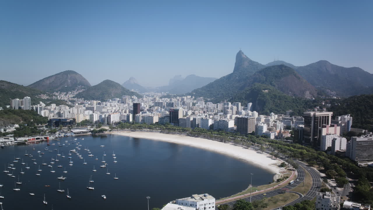 ariel time lapse de la playa de la bahía de botafogo con veleros y tráfico conduciendo durante el día con la estatua de cristo el redentor en el fondo en río de janeiro
