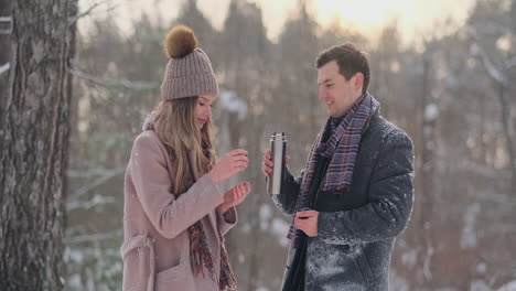 couple in love in the winter forest to drink tea from a thermos. stylish man and woman in a coat in the park in winter for a walk.