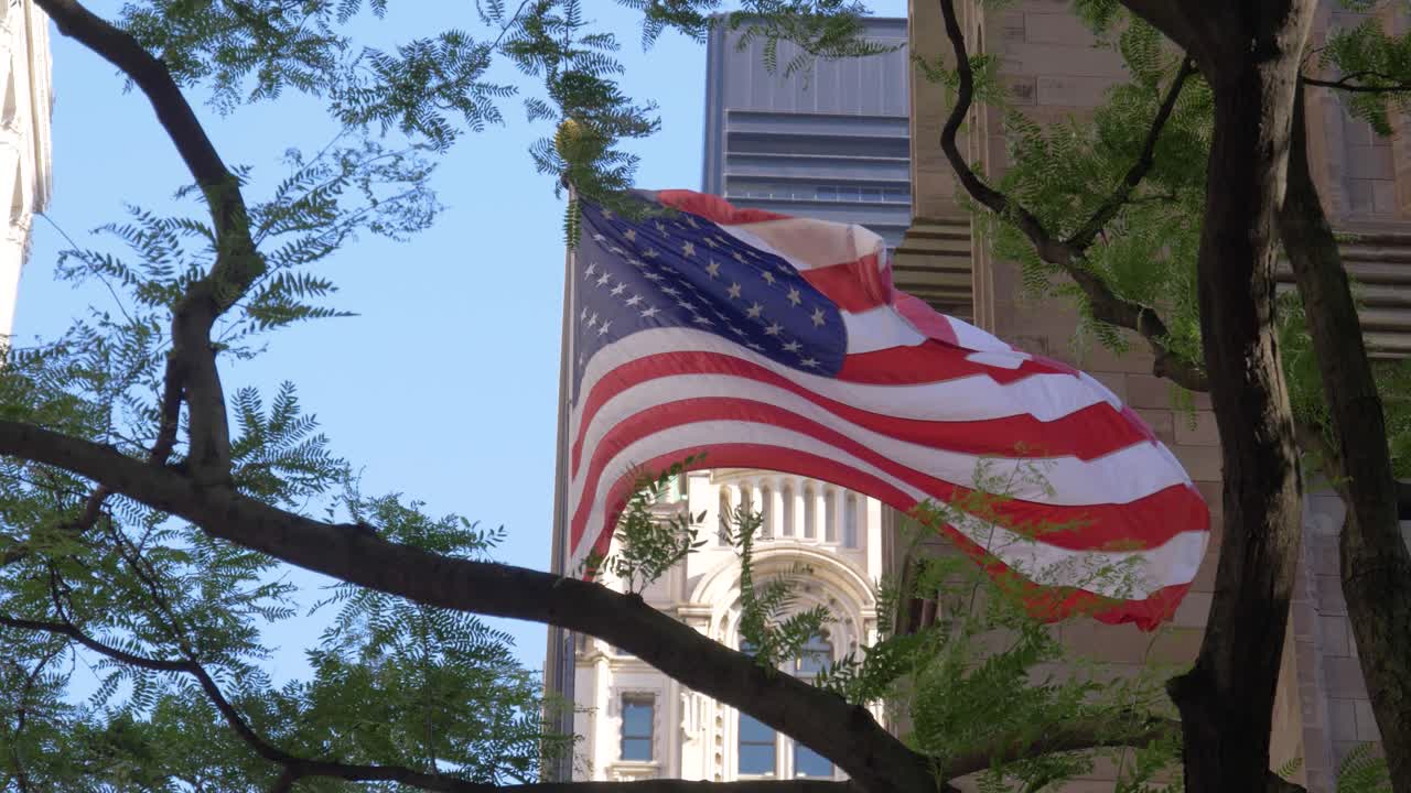 Ripresa al rallentatore della bandiera degli USA davanti alla Trinity Church, con alberi in primo piano, in estate a Manhattan, New York City.
