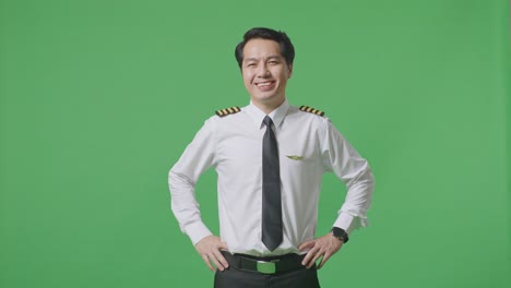 asian man pilot with arms akimbo looking at camera and smiling while standing in the green screen background studio