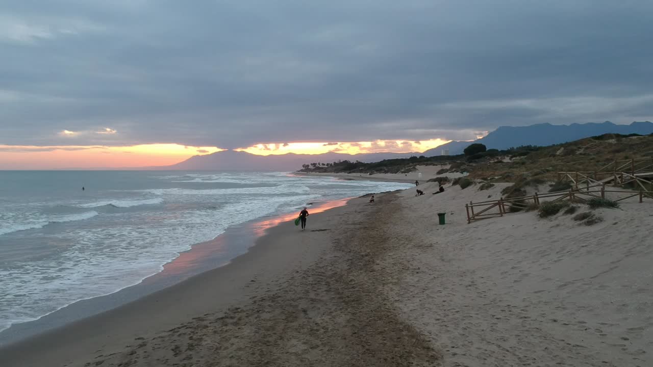vistas aéreas de una playa con un surfista corriendo por la playa