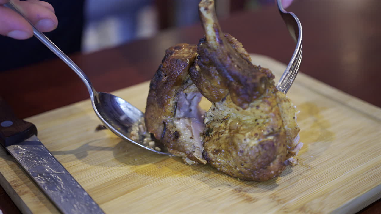 Close up of a man's hand cutting up a piece of pork on a wooden tray