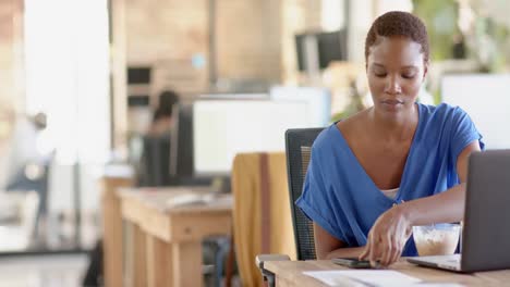 Happy-african-american-casual-businesswoman-using-smartphone-and-having-lunch-in-office,-slow-motion