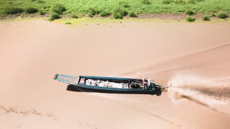 Aerial-drone-follow-fishing-boat-returning-churning-muddy-water-with-it's-long-shaft-outboard-from-this-immense-and-largest-fresh-water-lake,-the-Tonle-Sap,-South-East-Asia