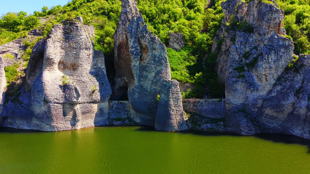Stenen doorgang bij water, Bulgarije. Smal pad tussen torenhoge rotswanden langs de rivieroever met twee zichtbare wandelaars.