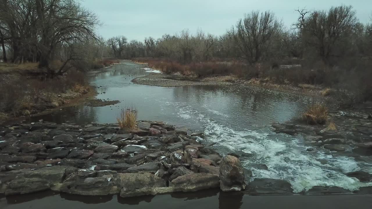Aerial: rocky weir on shallow section of mountain river in late autumn