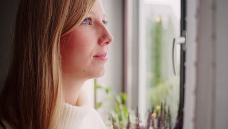 Schöne-Junge-Blonde-Frau,-Die-Aus-Dem-Fenster-Schaut-Und-Eine-Rote-Tasse-Kaffee-Hält