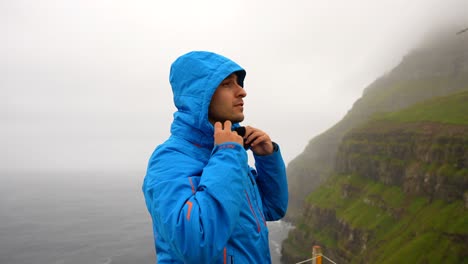 hombre atlético guapo levanta chaqueta de lluvia capucha para mantenerse seco explorando a lo largo de la costa de gasadalur