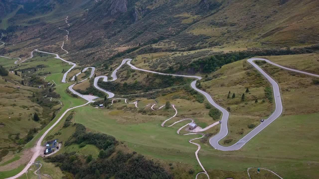 largo y sinuoso camino en la cordillera de los dolomitas en el norte de italia con autos que se mueven cerca del prado, tiro de revelación de drones aéreos