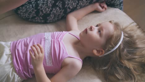 mother gives nose drops to little girl lying on soft bed