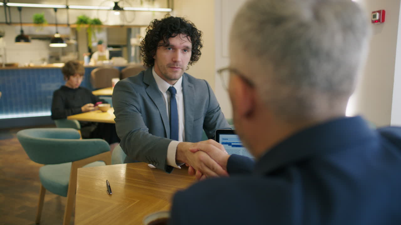 Businessman Shaking Hands and Discussing Document with Colleague in Cafe