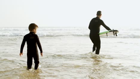 father and son with surfboard in water