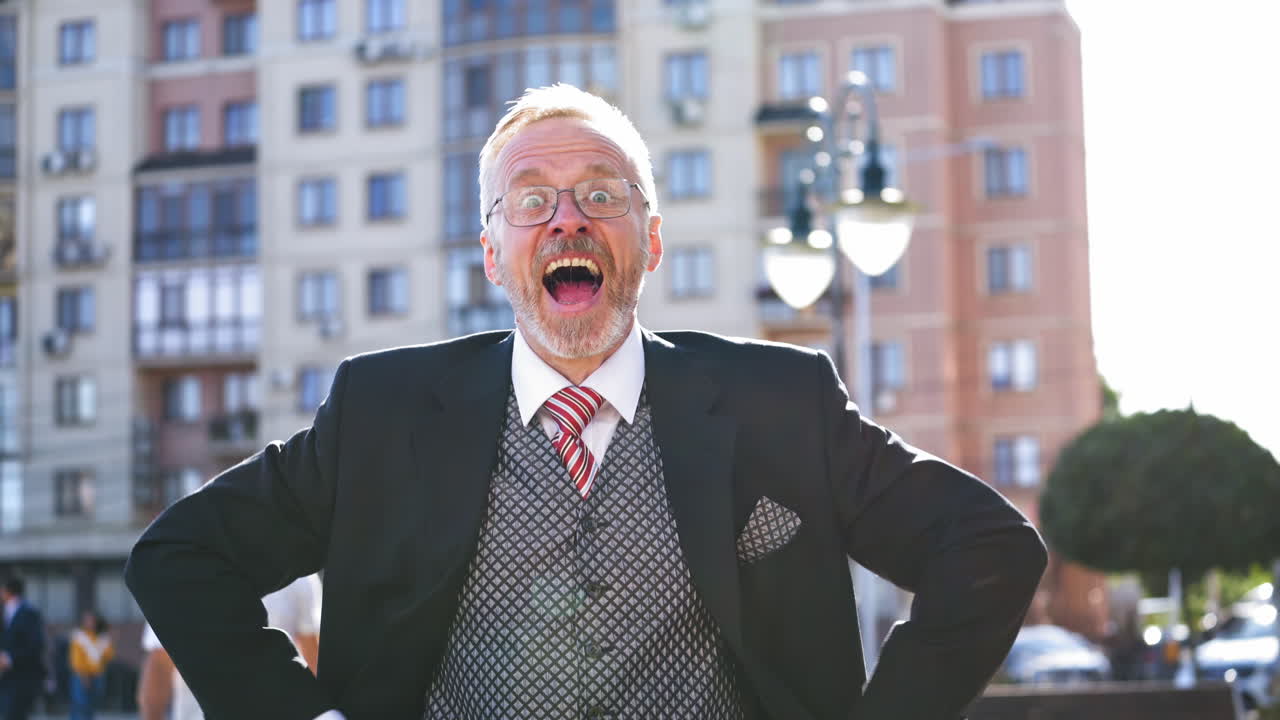 Senior businessman in glasses and suit talks happily on the city background. Enthusiastic middle aged man talking and showing happy gesture with his arms.