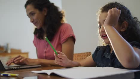 Happy-mixed-race-mother-and-daughter-doing-homework-and-working-on-laptop-at-home