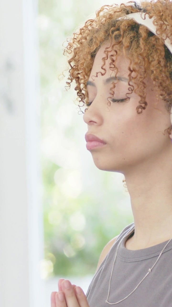 Vertical video: Closing eyes woman meditating at home by window, grey top, headset, copy space