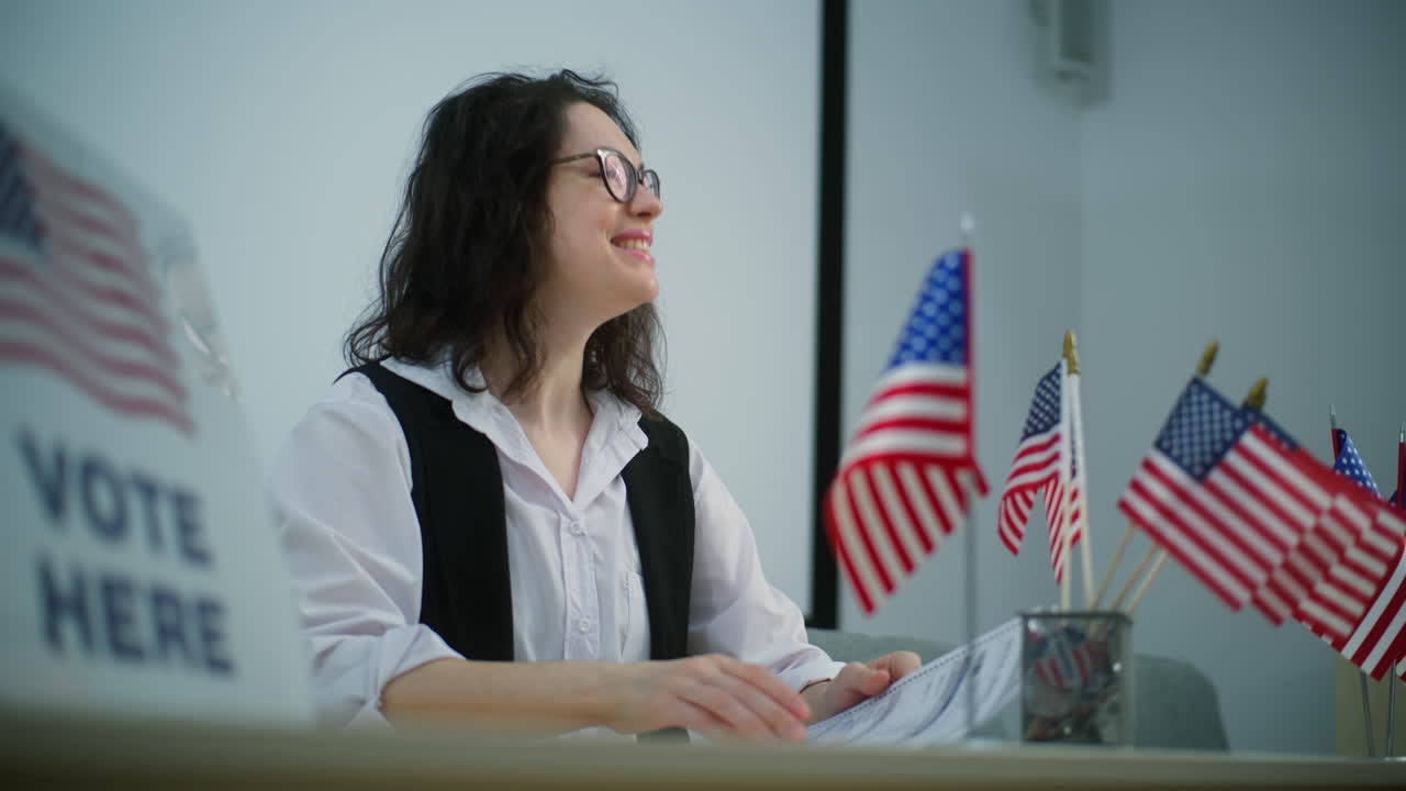 Female Polling Officer Talks with Person about Registration on Voting Female Polling Officer Sits at the Table with American Flags at Polling Station Talks with Person about Registration on Voting National Election Day in the United States Civic Duty and Democracy