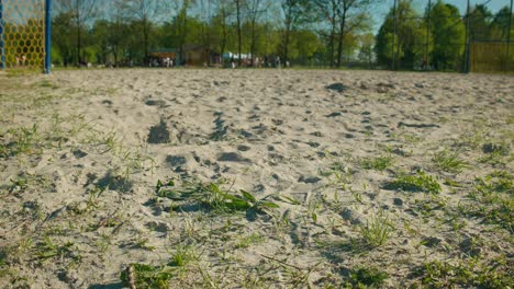 Close-up-view-of-a-sandy-football-court-with-a-goalpost-at-Jarun-Lake-in-Zagreb,-Croatia,-surrounded-by-greenery-and-people-in-the-background